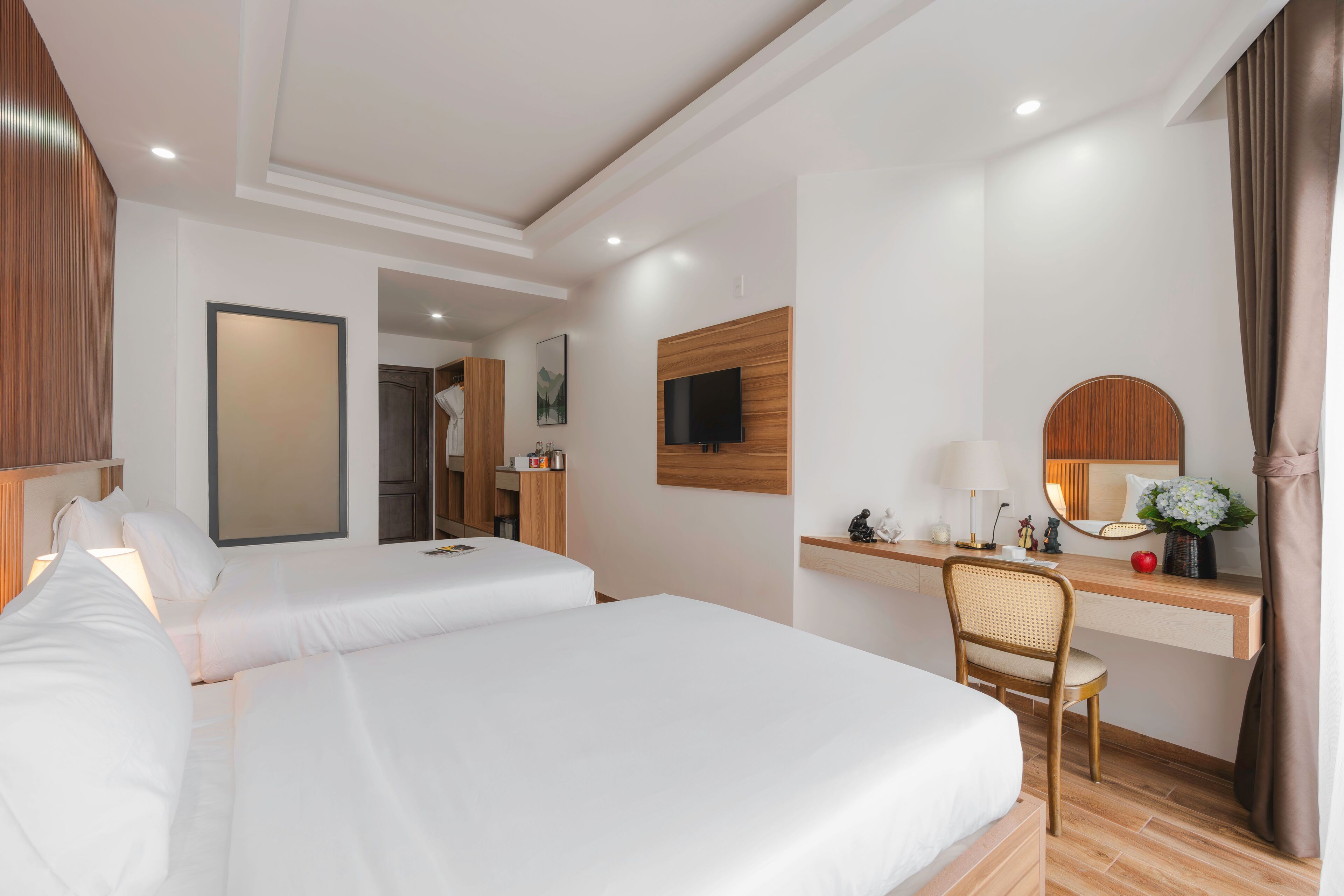 Quarto de hotel com duas camas, uma escrivaninha, uma cadeira, uma televisão e um espelho.