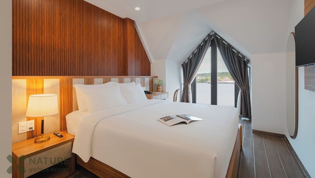 A hotel room with a large bed, a nightstand with a lamp, a bedside table with a phone, and a window with curtains.