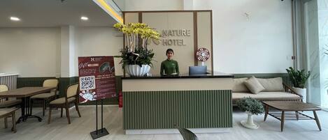 Ett receptionsområde med en receptionsdisk, en sittgrupp med en soffa och stolar, en stor krukväxt och en skylt för Nature Hotel.