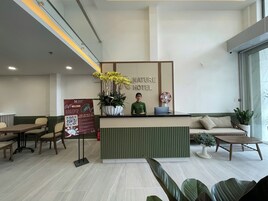 Un área de recepción con mostrador, zona de estar con sofá y sillones, una planta grande en maceta y un cartel que dice Nature Hotel.