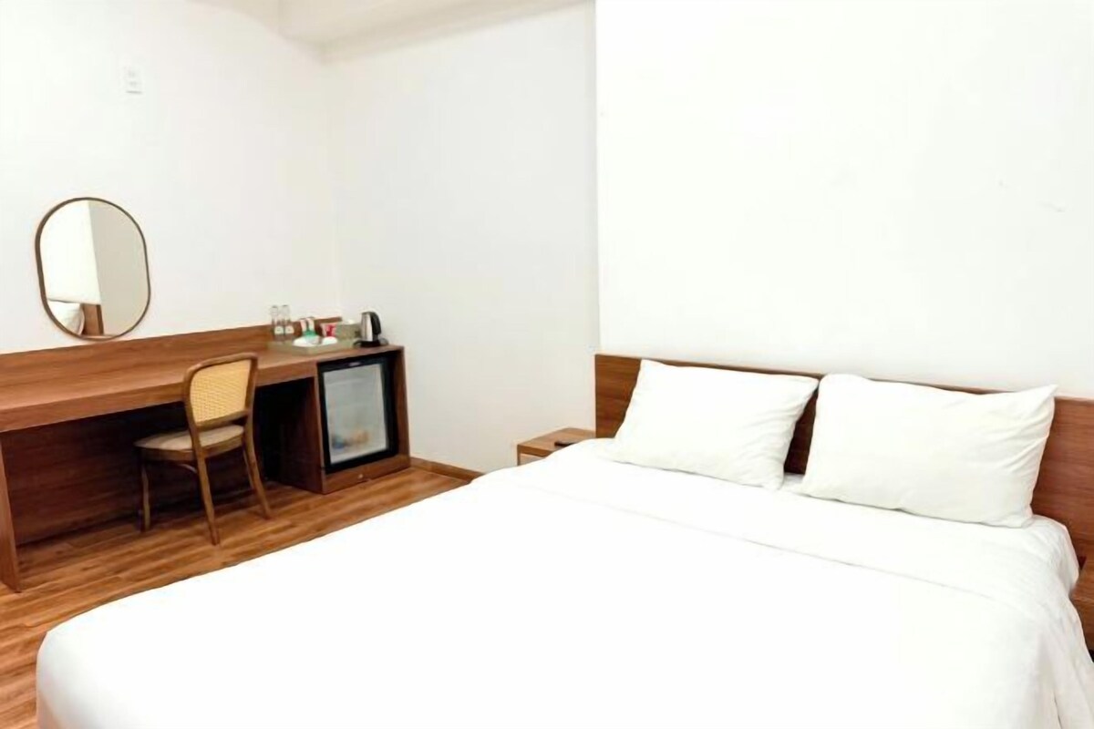 A hotel room with a bed, a wooden desk, a chair, a small TV, and a mirror.