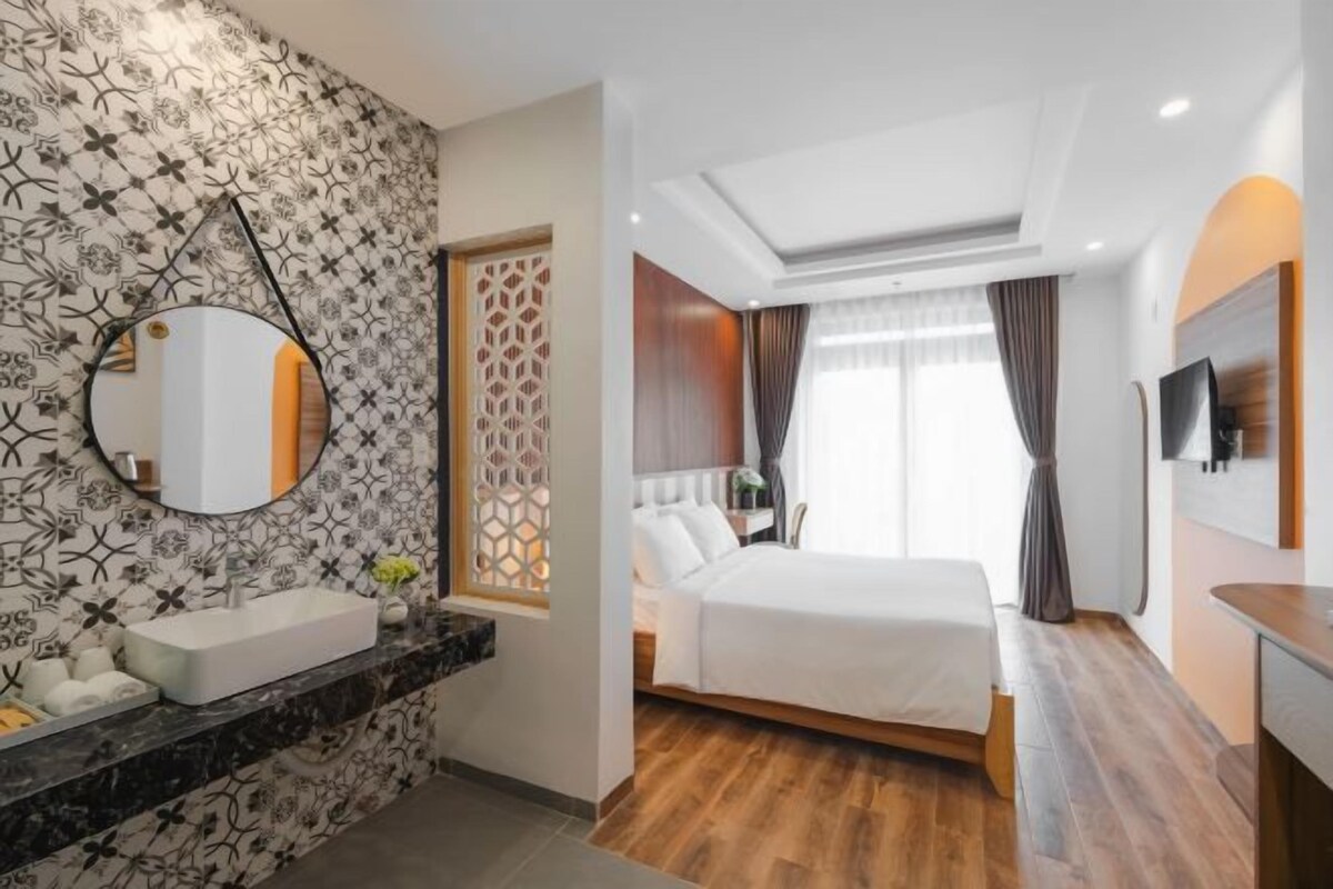 Ett modernt hotellrum med en stor säng, en rund spegel, ett badrum med handfat och en dekorativ vägg.