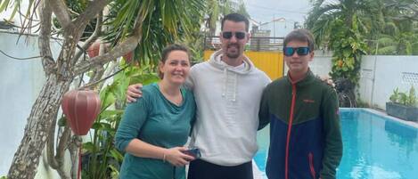 Three people standing by a pool with a tree and a fence in the background.