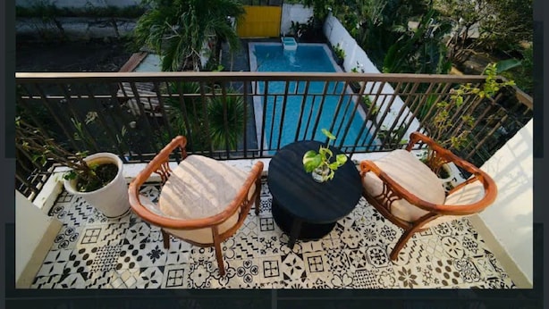 Un balcon avec deux chaises en bois et une petite table, une piscine et de la verdure tout autour.