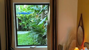 Une chambre d’hôtel avec un lit, une chaise, une fenêtre avec des rideaux, une lampe de chevet et une vue sur la verdure à l’extérieur.