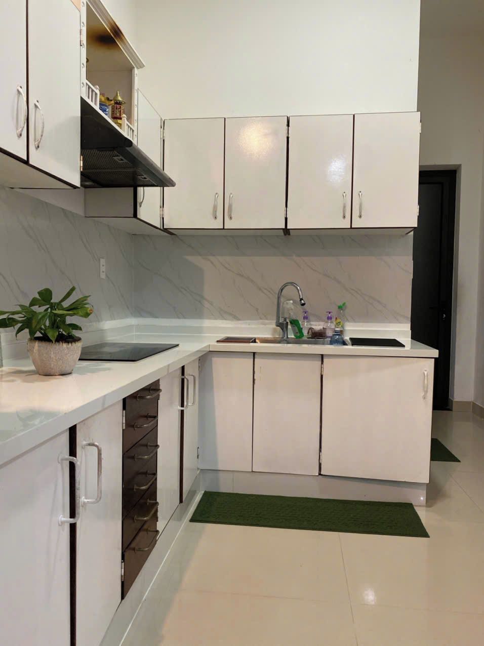 A modern kitchen with white cabinets, a marble backsplash, a sink, and a green rug.