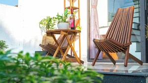 Una silla de madera y una mesita con una planta en maceta y una botella de vino en un balcón.