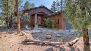 A rustic cabin with a stone entrance, wooden deck, and two Adirondack chairs.