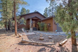 A rustic cabin with a stone entrance, wooden deck, and two Adirondack chairs. - Cozy Cabin in Beautiful Torreon (Show Low)