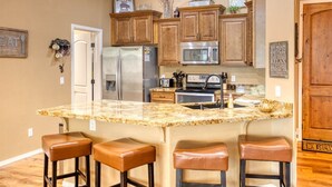 A kitchen with wooden cabinets, stainless steel appliances, a granite countertop, and three leather bar stools.
