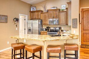 A kitchen with wooden cabinets, stainless steel appliances, a granite countertop, and three leather bar stools. - Cozy Cabin in Beautiful Torreon (Show Low)