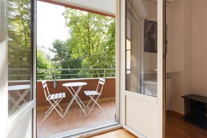 A balcony with a table and chairs, a view of trees, and a sliding glass door.