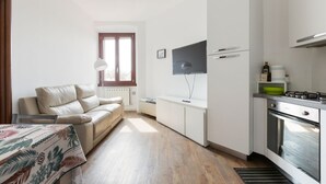 Um espaço compacto com cozinha compacta, sofá, televisão e janela.