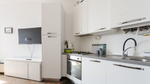 Cozinha moderna com armários brancos, fogão a gás, forno embutido e pia de aço inoxidável.