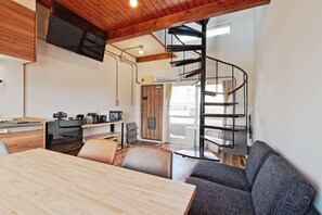 Eine moderne Küche mit Holzboden, ein Essbereich mit Holztisch und -stühlen sowie eine Wendeltreppe, die zu einer oberen Ebene führt.