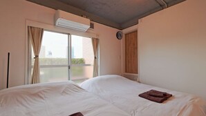 A bedroom with two beds, a window with curtains, an air conditioning unit, and a clock on the wall. - There are 1 bed room with 2 double beds (渋谷区)