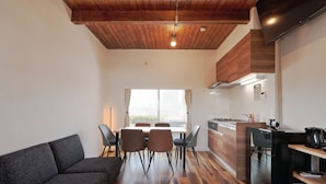 A modern living room with a sofa, dining table, and chairs, a kitchen with a stove and sink, and a large window providing natural light. - There are 1 bed room with 2 double beds (渋谷区)
