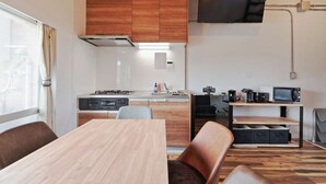 A modern kitchen with a built-in stove, microwave, and sink. There is a dining area with a wooden table and chairs. - There are 1 bed room with 2 double beds (渋谷区)