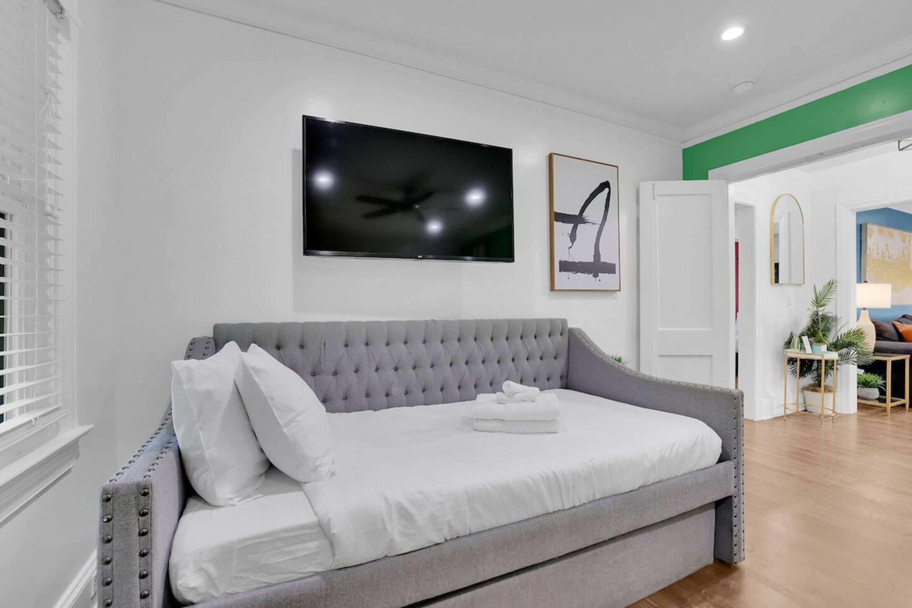 Une chambre moderne avec un canapé-lit gris, un téléviseur à écran plat et une œuvre d’art encadrée accrochée au mur.