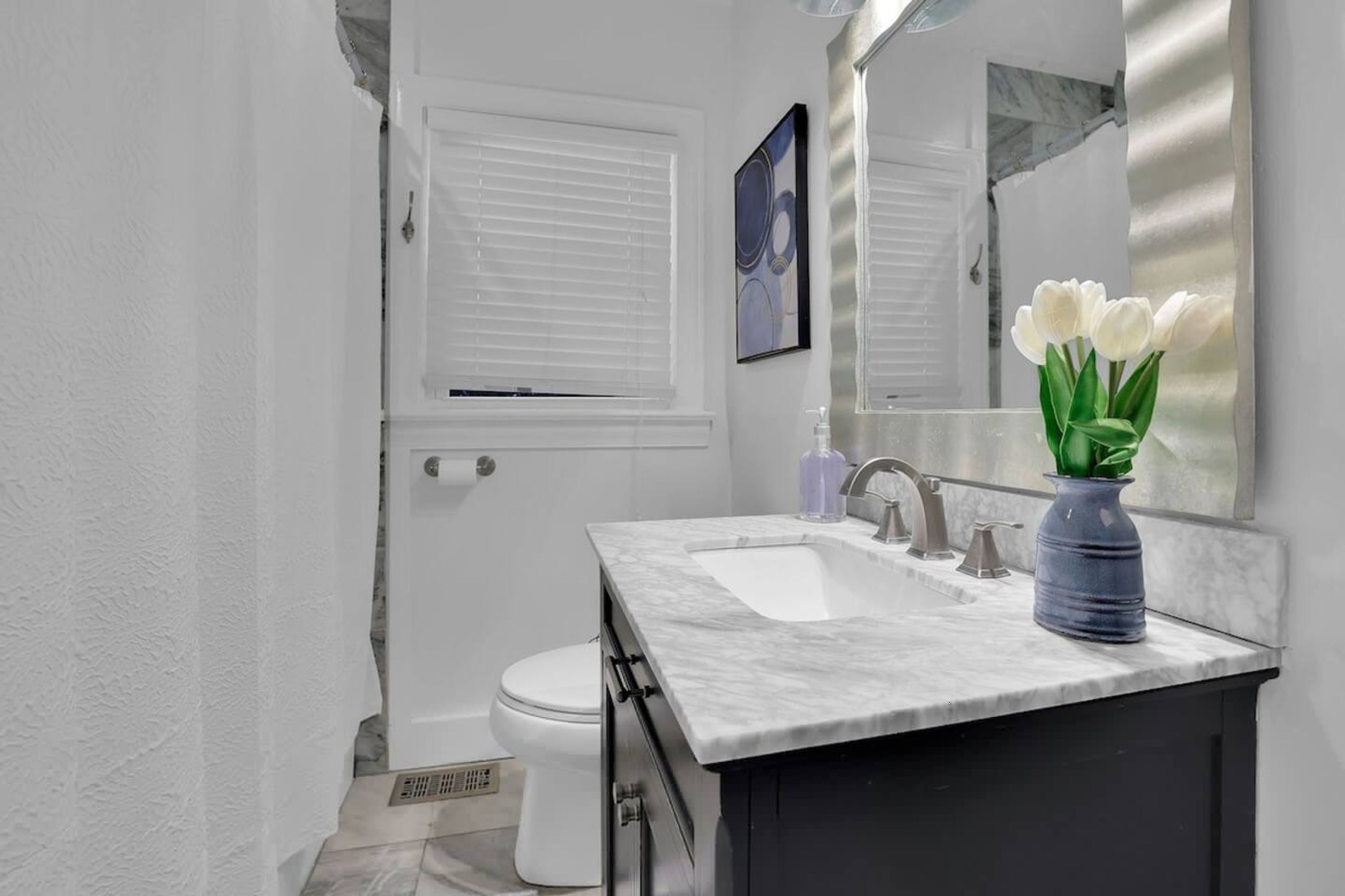 A modern bathroom with a white sink, dark cabinet, and a vase of white flowers.