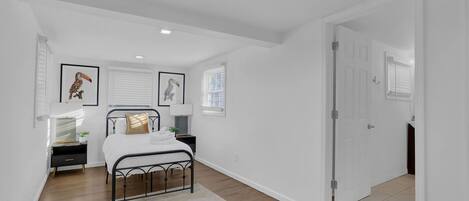 Un dormitorio con cama, mesitas de noche, una ventana con persianas y una puerta.