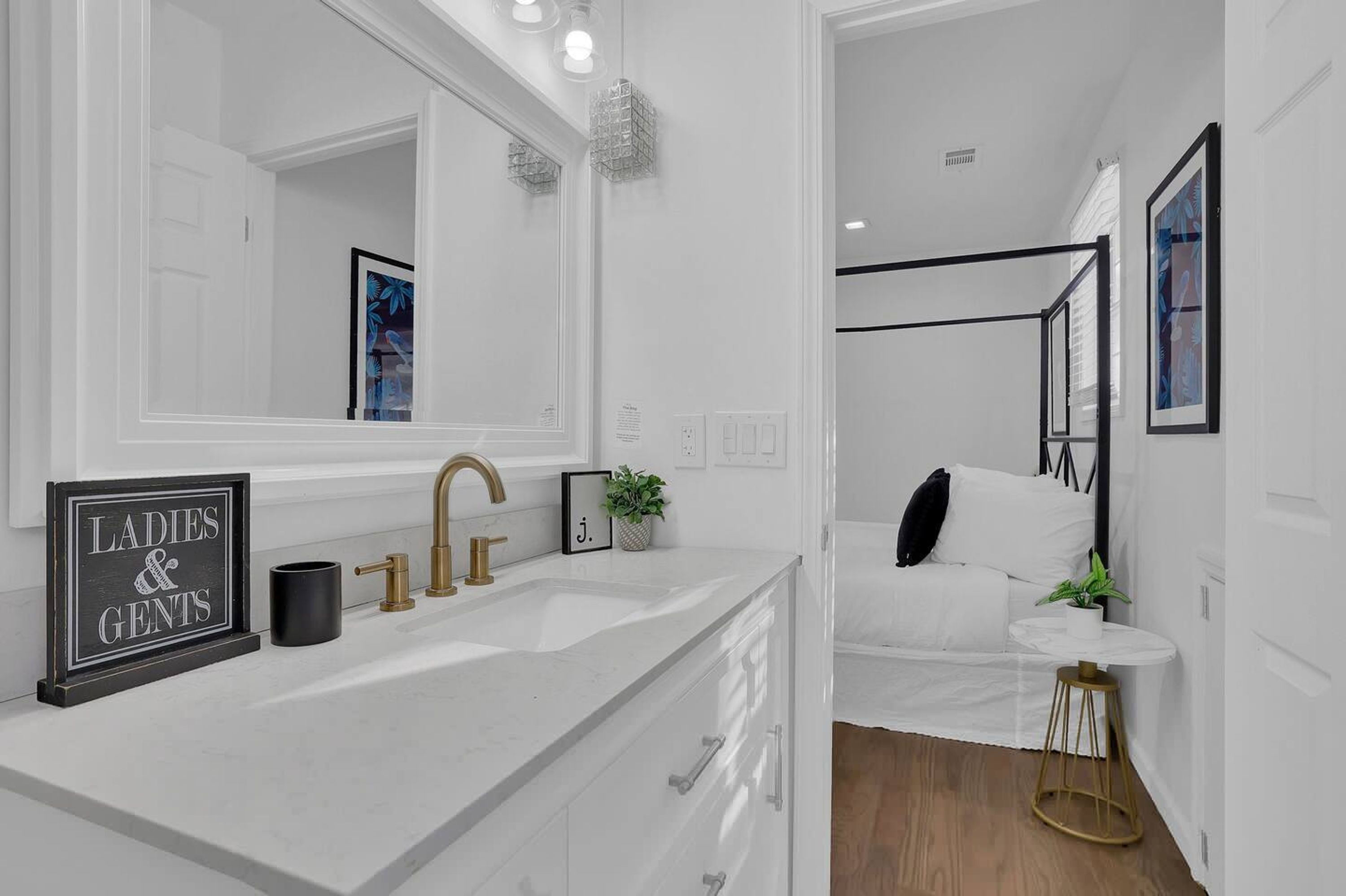 A modern bathroom with a large mirror, a sink with gold fixtures, and a framed sign on the counter.