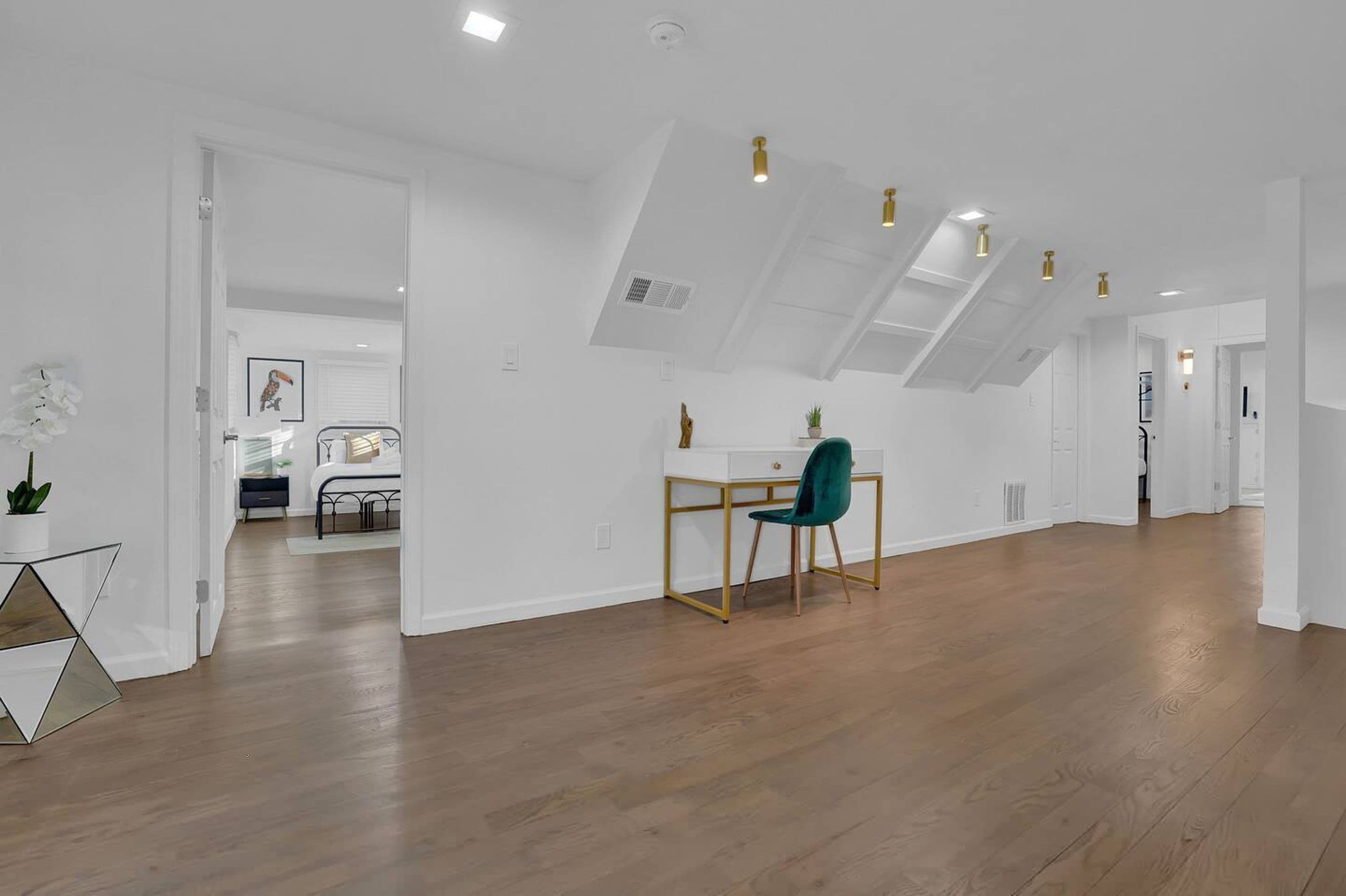 Une pièce spacieuse avec un plancher en bois, un bureau avec une chaise et une lucarne.