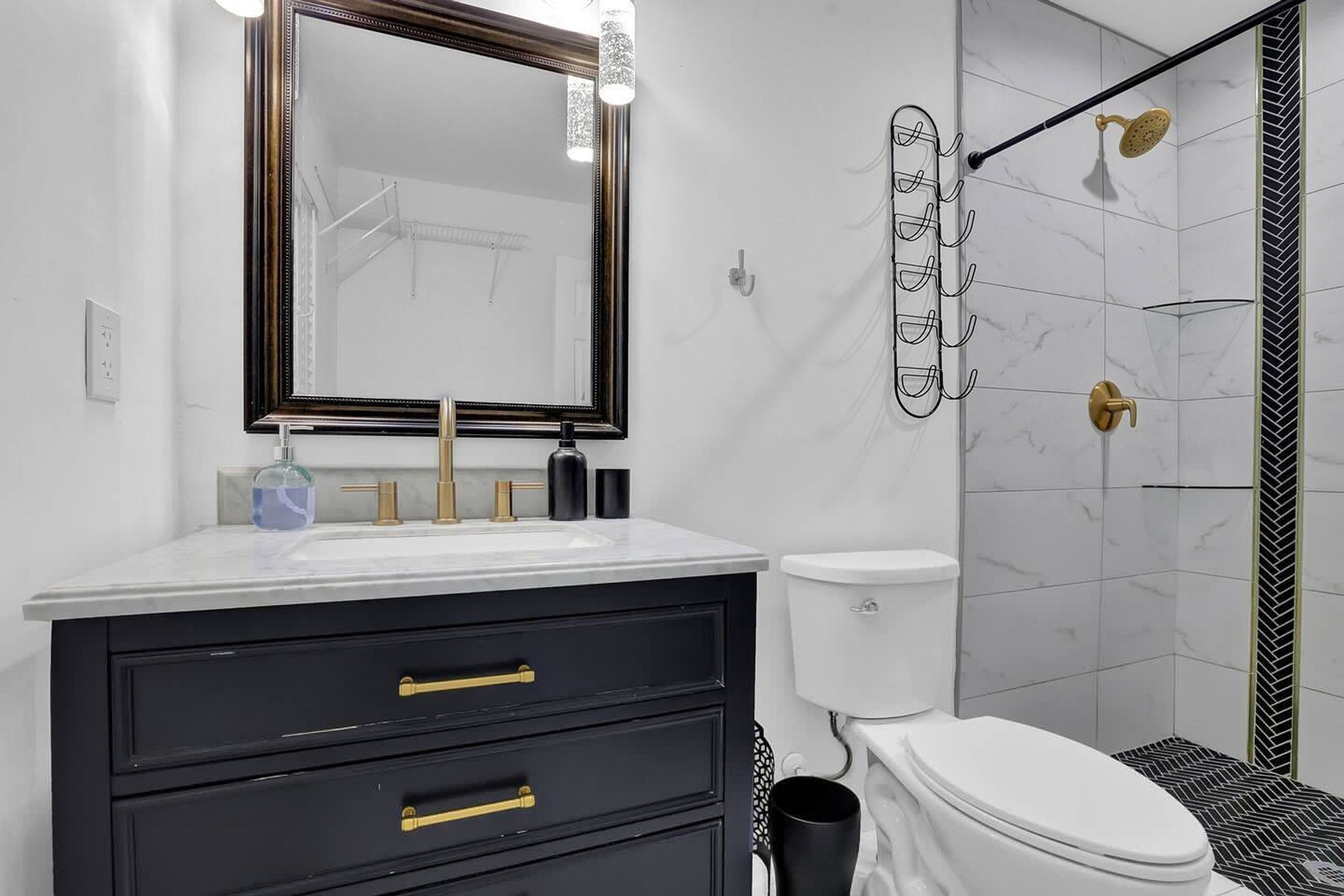 A modern bathroom with a white sink, black vanity, gold fixtures, and a shower with a black and white herringbone tile backsplash.
