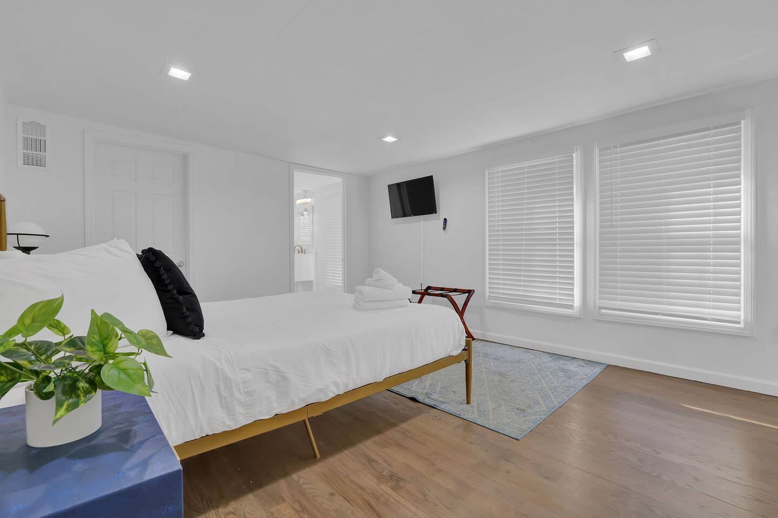 Une chambre à coucher avec un lit, une télévision, des murs blancs et une fenêtre avec des stores.