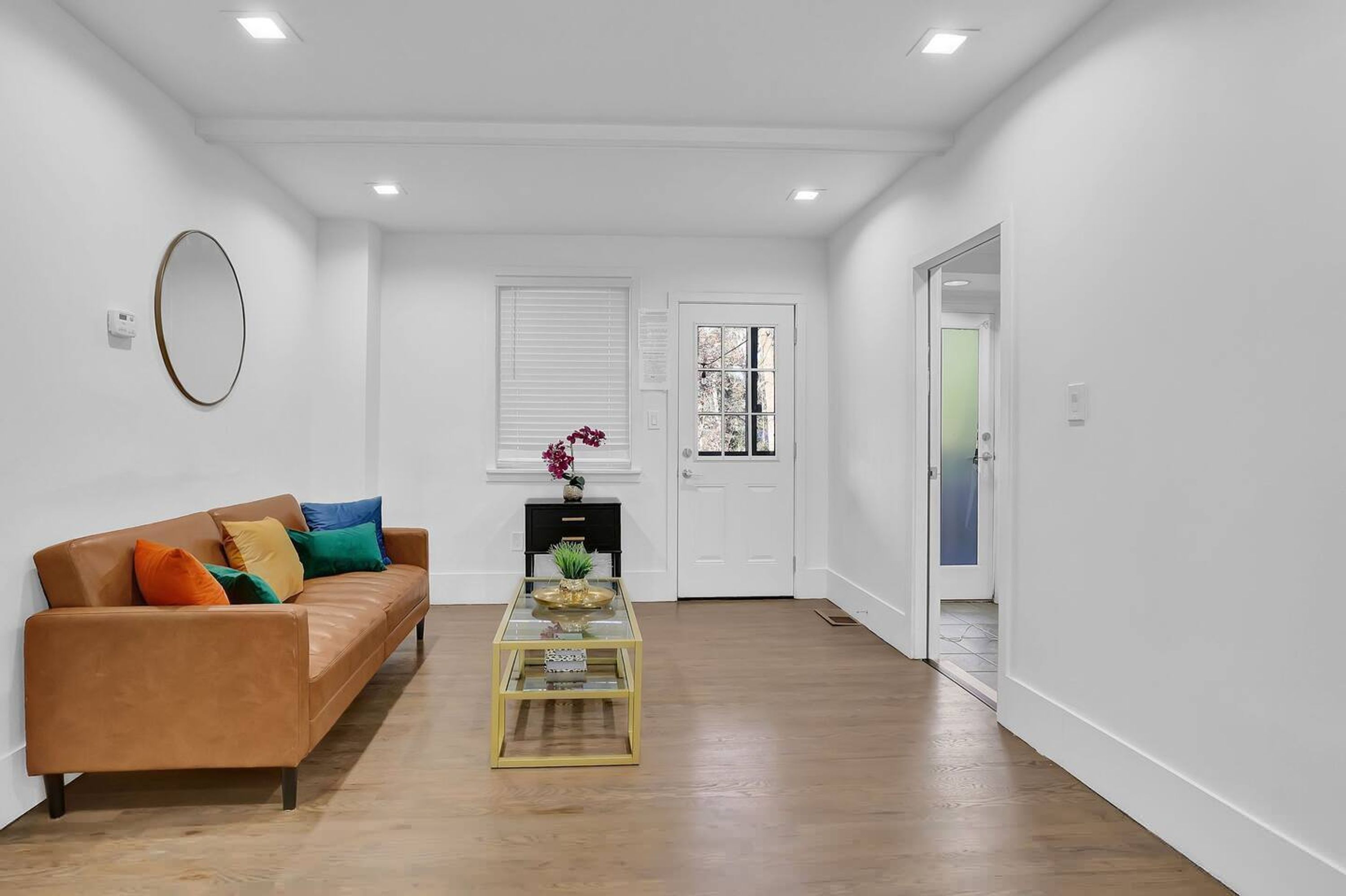 A modern living room with a brown leather sofa, a glass coffee table, and a white door in the background.