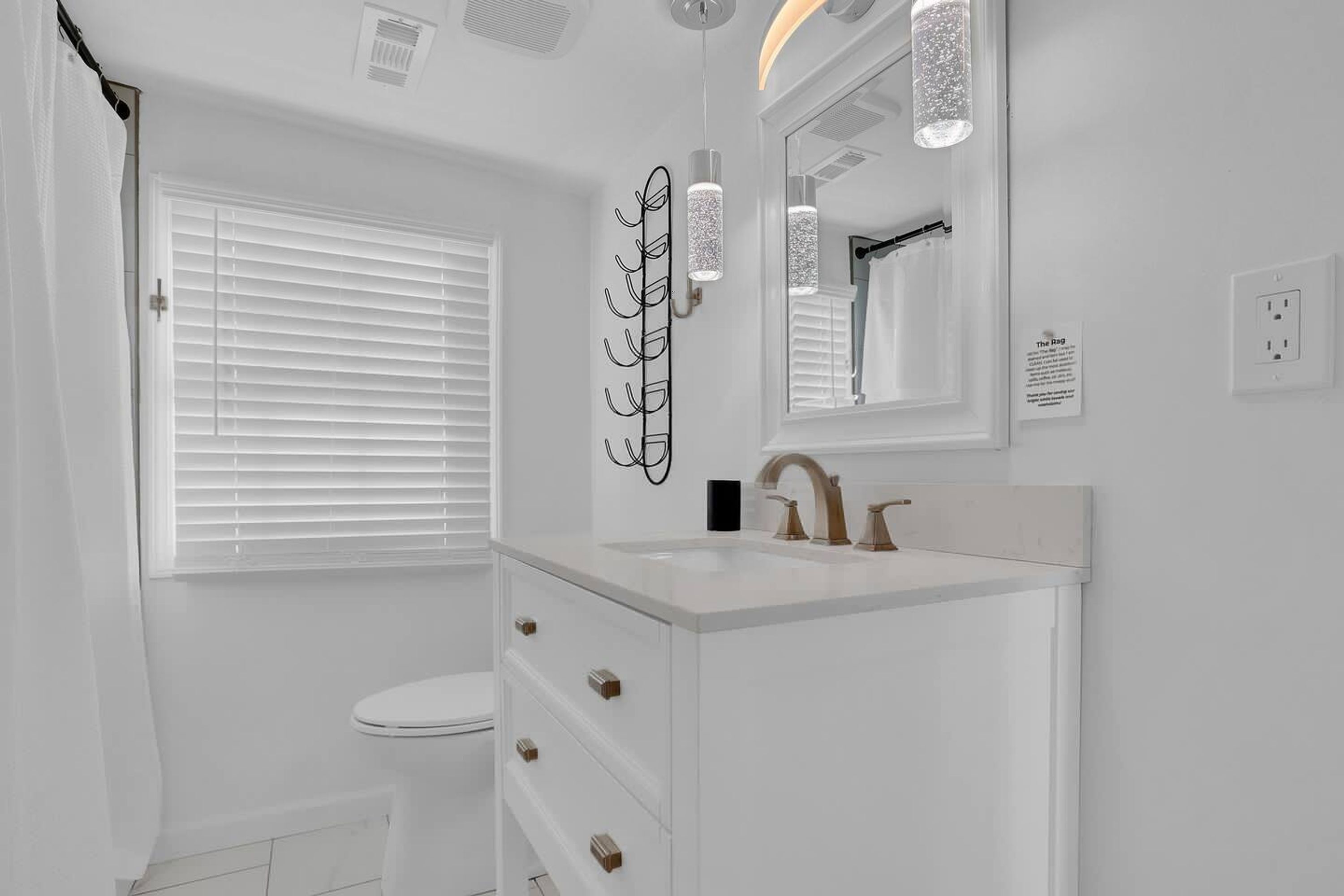 Une salle de bain moderne avec un meuble-lavabo blanc, des toilettes et une fenêtre équipée de stores.