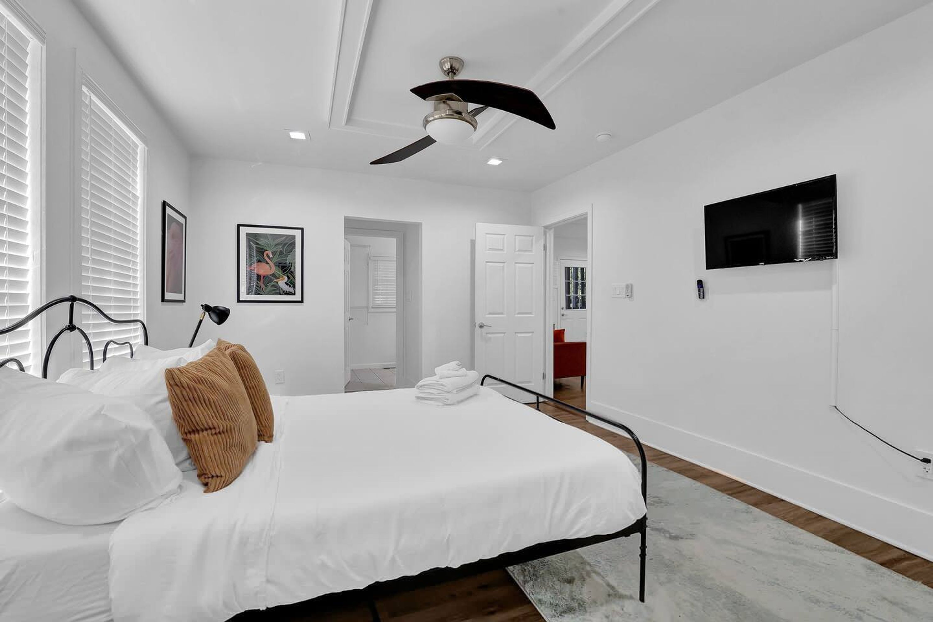Een slaapkamer met een bed, plafondventilator, witte muren en een televisie aan de muur.