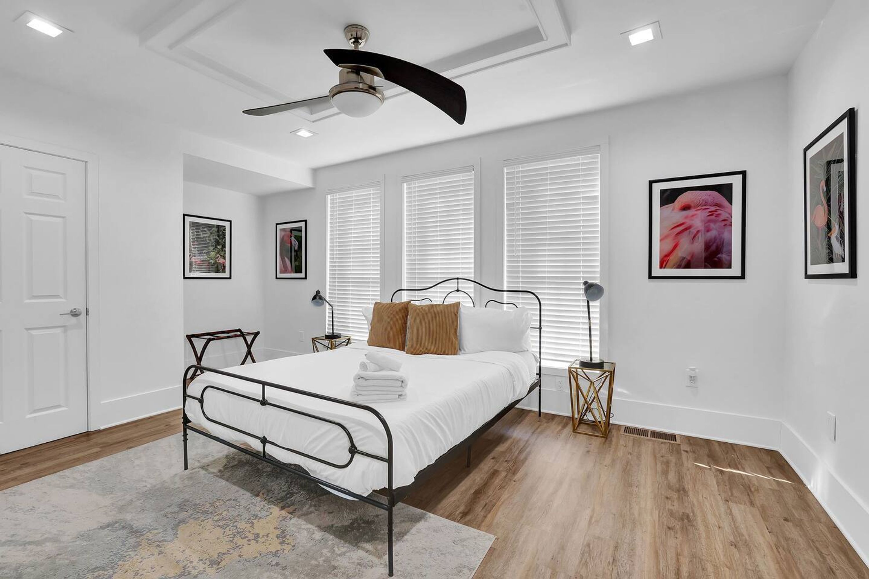 A bedroom with a bed, white walls, a ceiling fan, and framed pictures.