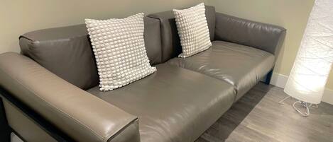 A brown leather sofa with two white textured pillows.
