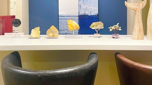 Un mostrador de recepción con pared azul, un cuadro abstracto grande y varios objetos decorativos, incluyendo cristales y una escultura de madera.
