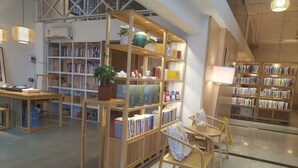 A bookstore with wooden shelves, a central table with a plant, and a staircase in the background. - JINJU ART HOTEL (Guangzhou)