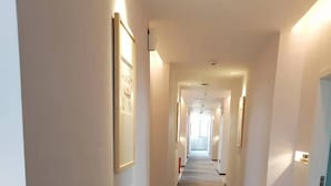 A long, narrow hotel corridor with a dark carpet, white walls, and framed pictures on the left. - JINJU ART HOTEL (Guangzhou)