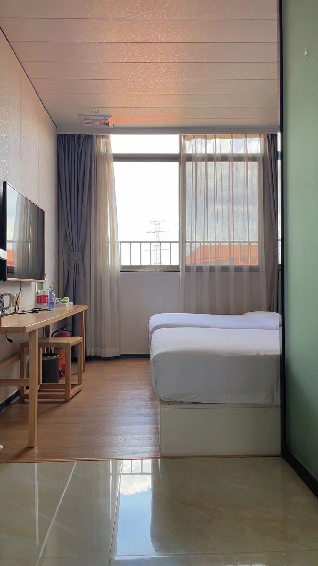 A hotel room with a bed, a TV, a desk, and a window with curtains.