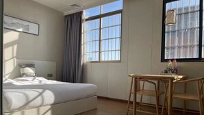 A bedroom with a bed, a desk with chairs, a window with curtains, and a hanging light fixture. - JINJU ART HOTEL (Guangzhou)