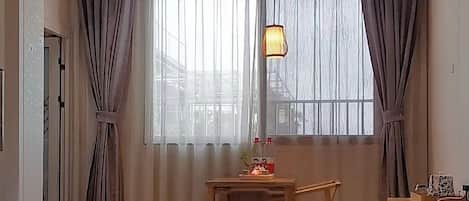 Una habitación de hotel con una cama grande, un escritorio de madera, una lámpara colgante y un ventanal con cortinas.