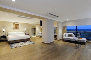 A modern hotel room with a large bed, a sofa, a dining area, and a view of the city at dusk. - Ginger Hyderabad Airport Road (Hyderabad)