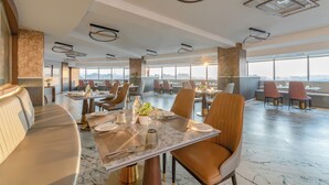 A modern restaurant with marble flooring, leather seating, and large windows offering a city view. - Ginger Hyderabad Airport Road (Hyderabad)