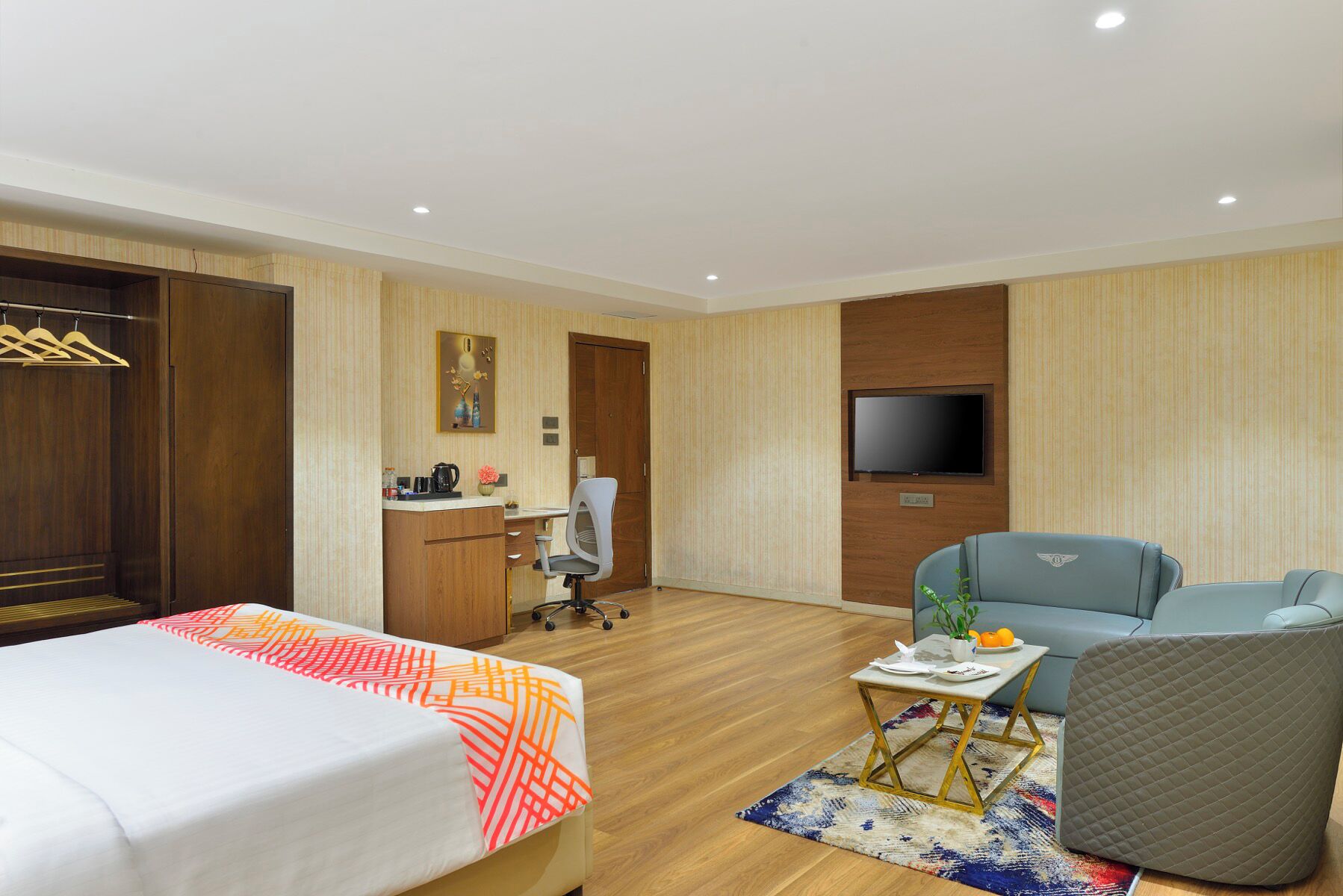 A hotel room with two beds, a desk, a chair, a sofa, a television, and a small table with a plant.