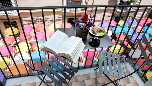 Un balcón con una mesa dispuesta para una comida, un libro y un jarrón con flores.