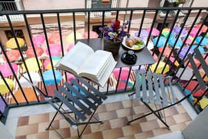 Un balcone con un tavolo apparecchiato per un pasto, un libro e un vaso di fiori.