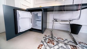 Cocina compacta con refrigerador integrado, una silla transparente y piso de baldosas.