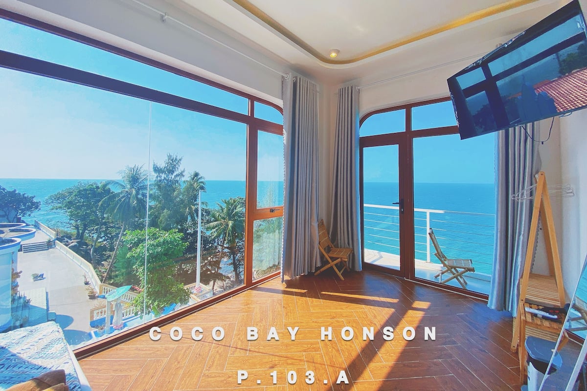 A spacious room with large windows offering a view of the ocean and palm trees.