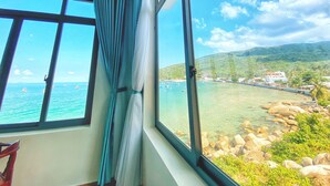 A room with a large window overlooking a coastal area with boats and rocky shores. - Coco Bay Hòn Sơn (Kien Hai)