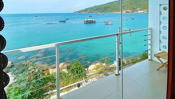 A balcony with a view of the sea, featuring boats and a hilly landscape in the background. - Coco Bay Hòn Sơn (Kien Hai)