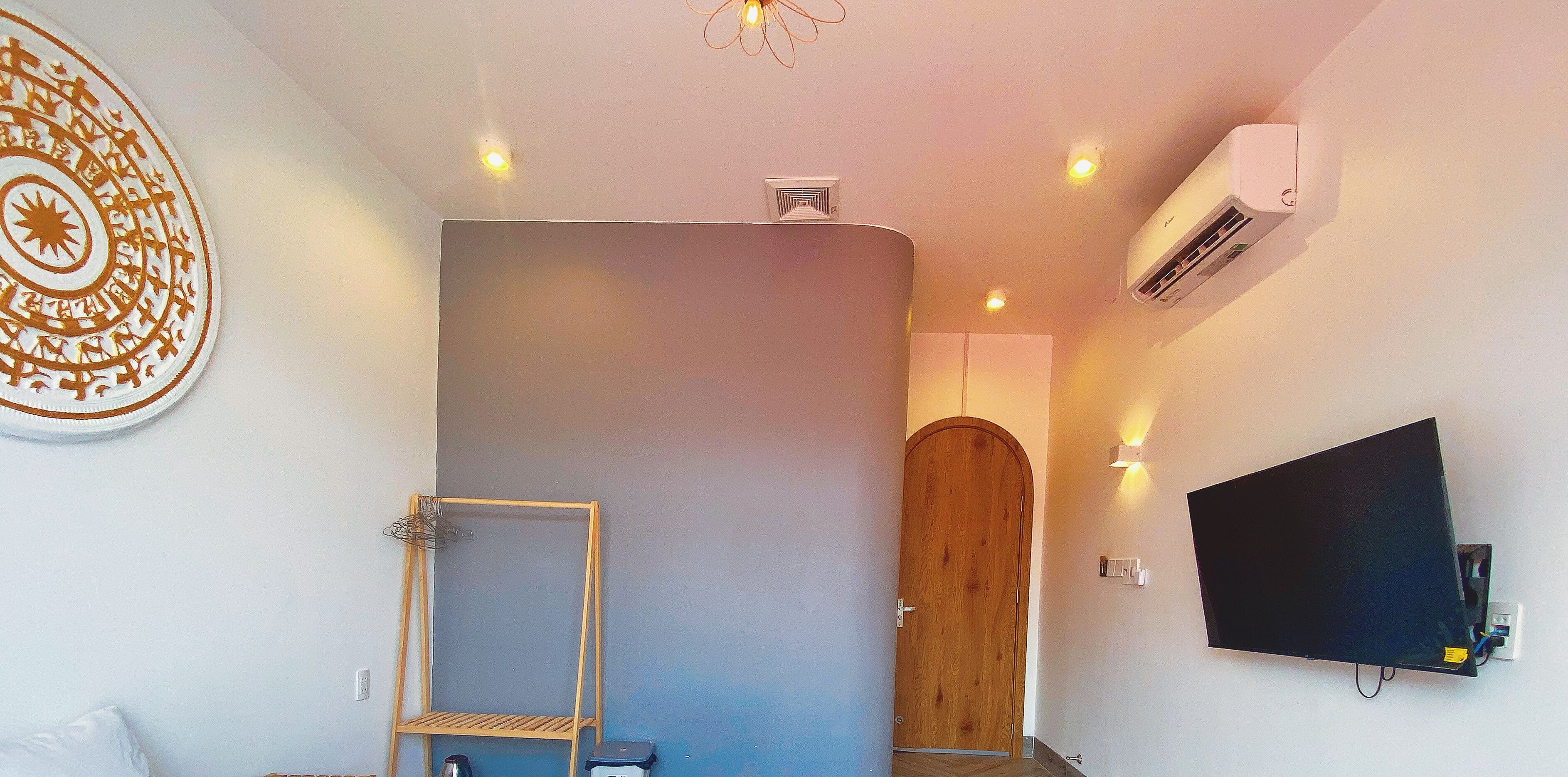 Une pièce avec une porte en bois, un téléviseur fixé au mur et un luminaire au plafond.